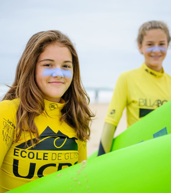 Adolescents en tenue UCPA avec planches de surf verte à la plage pour un séjour surf et padel