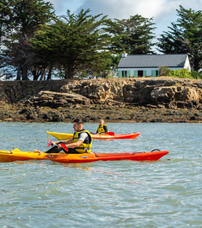 Enfants en kayak et paddle colorés dans le Golfe du Morbihan avec rochers et végétation côtière