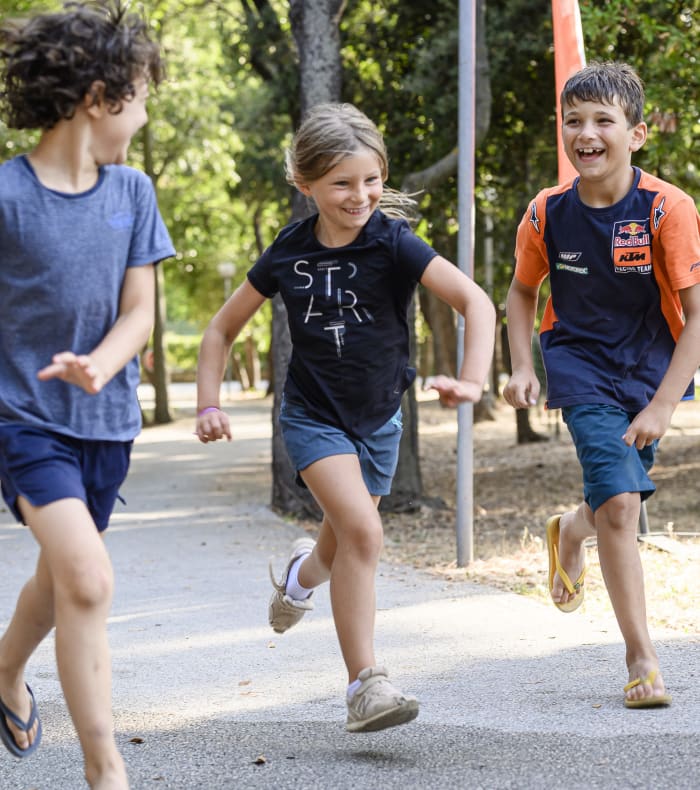 Trois enfants courant ensemble sur un sentier en forêt méditerranéenne lors du séjour multisports Toussaint à Saint-Cyr-sur-Mer