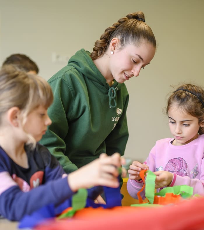 Animatrice en colonie de vacances accompagnant des enfants lors d'une activité créative avec des blocs de couleur