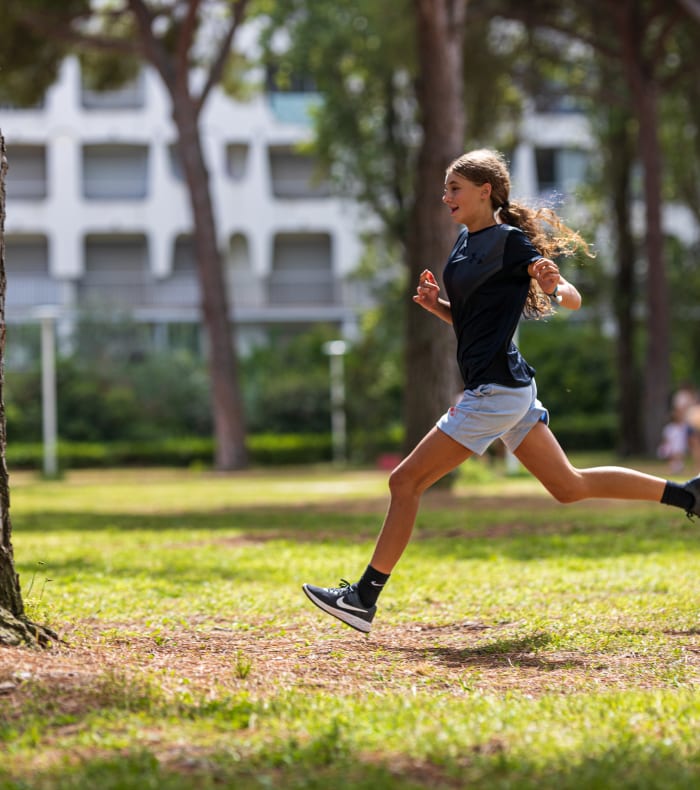 Femme jogging dans un parc verdoyant avec grands arbres et bâtiment en arrière-plan lors d'une formation générale de 8 jours
