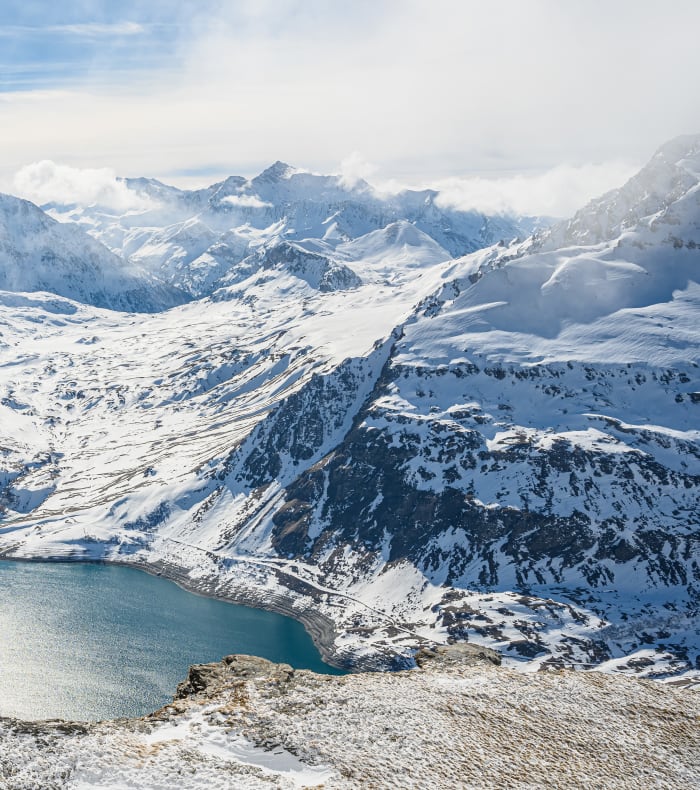 Panorama enneigé de Val Cenis avec lac alpin turquoise et chaîne de montagnes rocheuses en arrière-plan