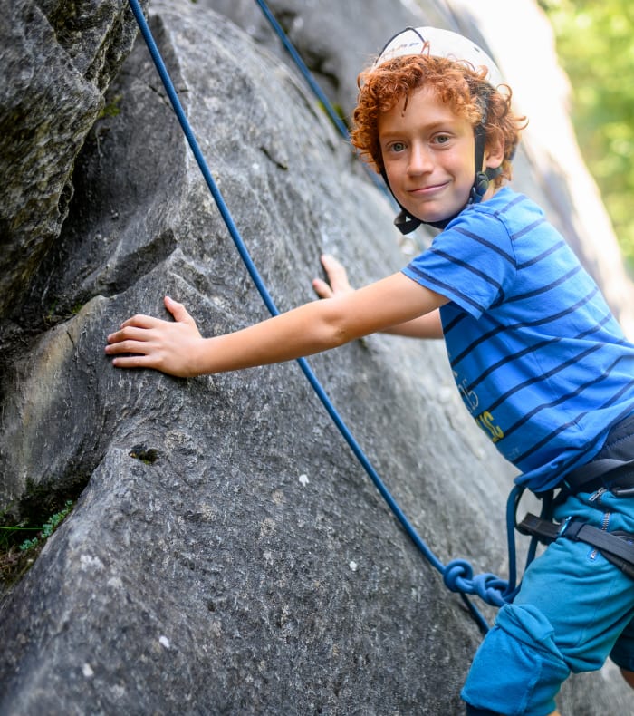 Enfant pratiquant l'escalade sur paroi rocheuse avec baudrier et casque de protection en montagne