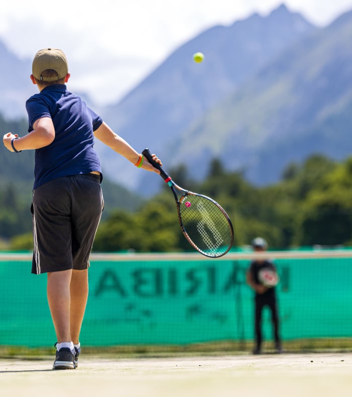 Enfant jouant au tennis en montagne à Valloire avec raquette et balles sur court en terre battue