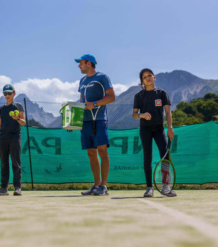 Jeunes enfants en tenue de tennis posant sur un court avec raquettes et balles, montagnes en arrière-plan