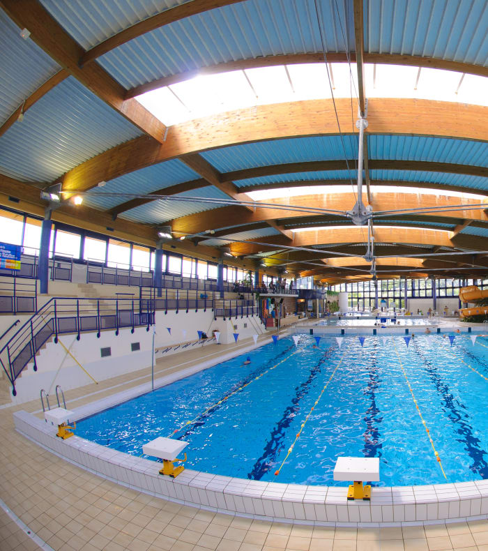 Piscine couverte avec bassin olympique aux couloirs délimités, architecture moderne avec verrière lumineuse et équipements de surveillance