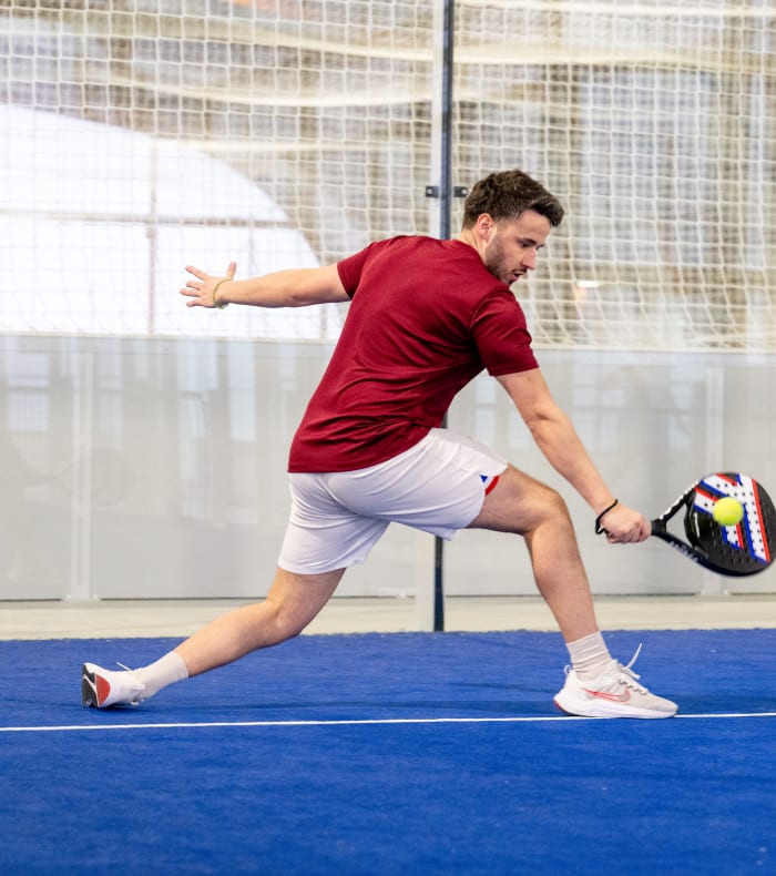 Joueur en position offensive sur court de padel avec raquette et balle, illustration de l'activité padel proposée