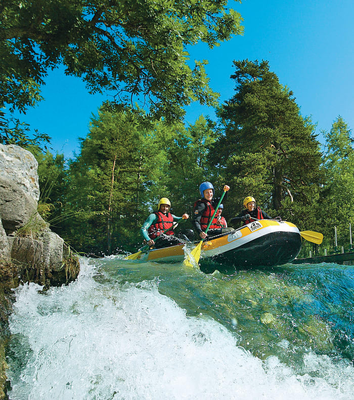 Groupe en rafting sur eaux vives turquoise entouré de forêt alpine et montagnes sous ciel bleu