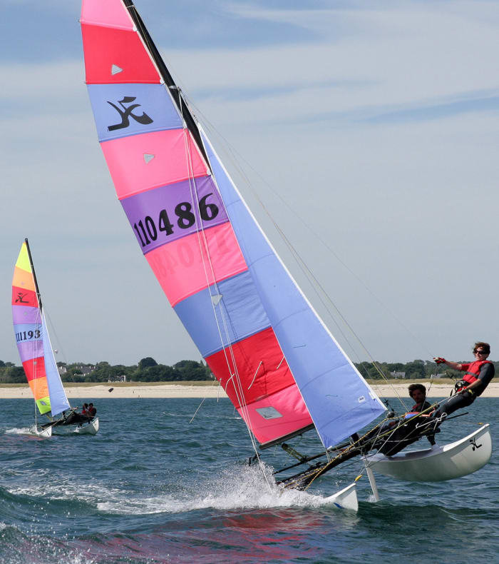 Catamarans de performance avec voiles roses et bleues navigant en mer lors d'un séjour de voile en Bretagne