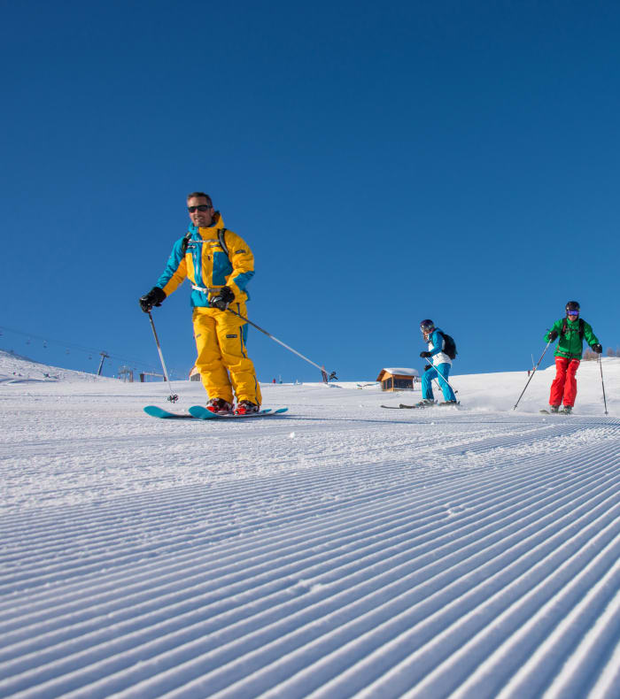 Moniteur en tenue jaune enseignant le ski à un groupe d'enfants sur piste enneigée par beau temps