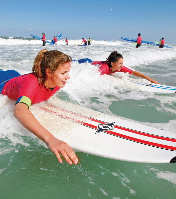 Adolescents en séance de surf dans l'océan à Lacanau, allongés sur leurs planches dans les vagues avec moniteurs en arrière-plan