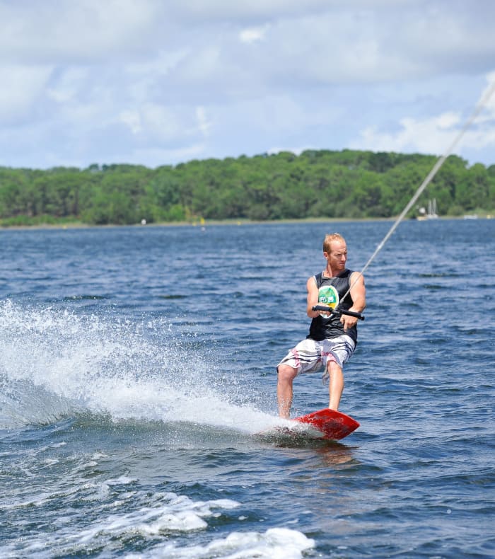 Wakeboarder en action sur le lac de Carcans avec gilet de sauvetage et forêt verdoyante en arrière-plan