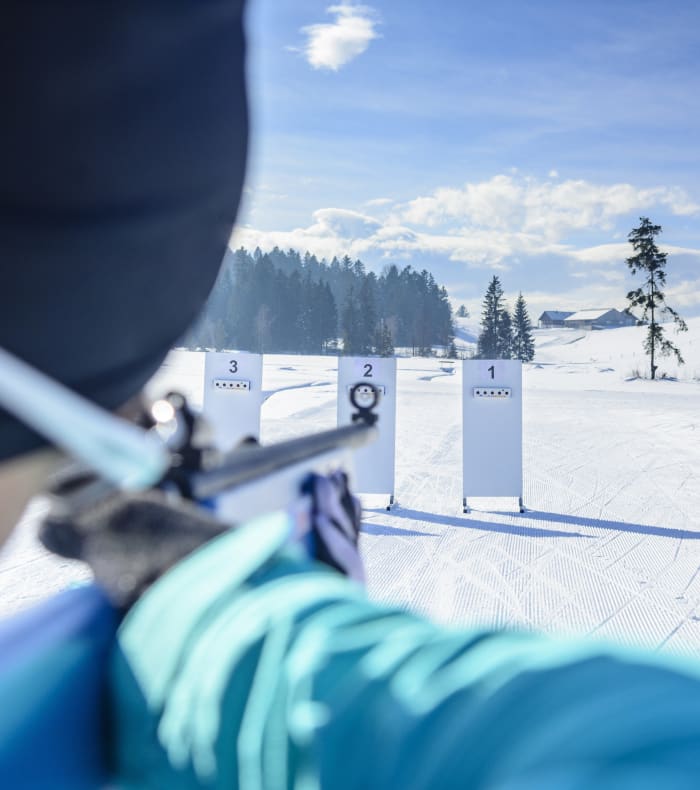 Biathlète en position de tir à plat ventre avec fusil de biathlon en forêt enneigée