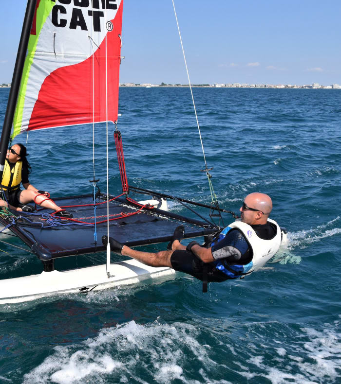 Catamaran avec voiles colorées et deux adultes en gilets de sauvetage naviguant en baie d'Aigues-Mortes