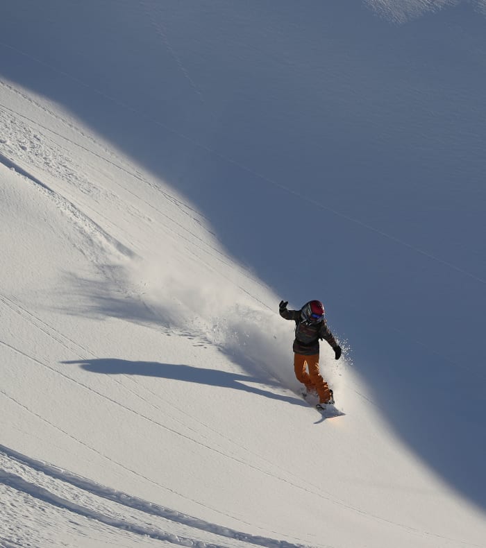 Snowboarder en descente hors-piste sur pente enneigée des Alpes avec poudreuse fraîche et ciel dégagé