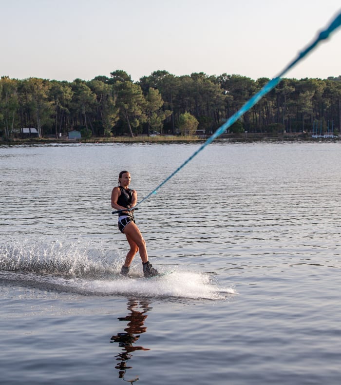 Windsurfeur en action sur le lac de Carcans avec voile bleue, plan d'eau abrité et forêt en arrière-plan