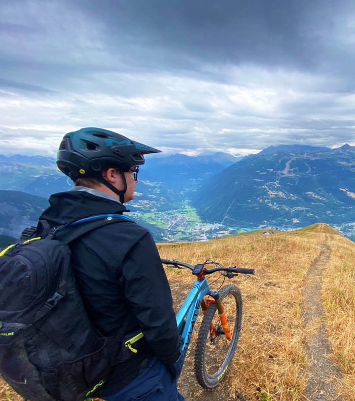 Vététiste en casque et sac à dos face à un single de montagne avec vue panoramique sur la vallée de Tarentaise et les Alpes