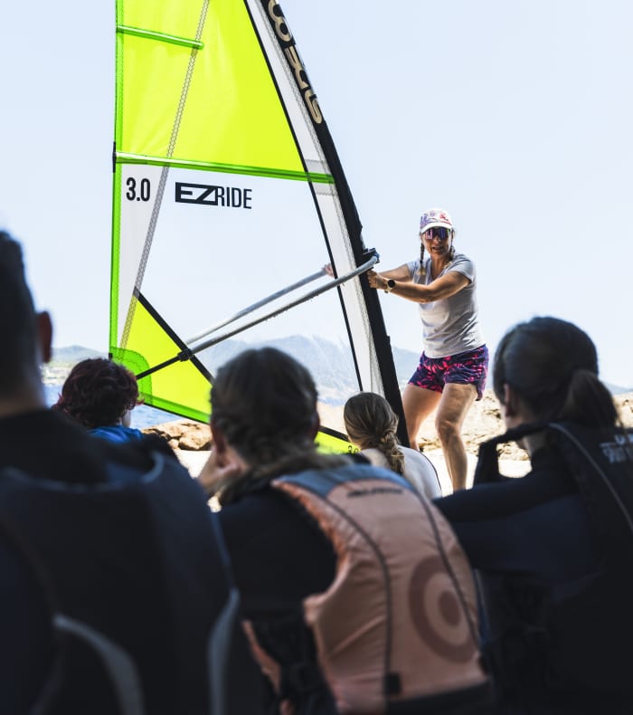 Moniteur de windsurf tenant une voile jaune fluo face à des stagiaires sur la plage lors du stage Brea 4 jours
