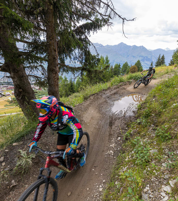 Cycliste en VTT saluant en l'air sur un sentier de bikepark avec terrain boisé en arrière-plan