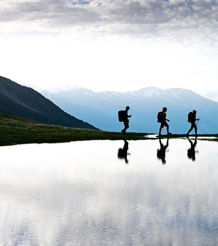 Groupe de randonneurs en itinérance dans les Écrins avec sommets enneigés et lac alpin en réflexion