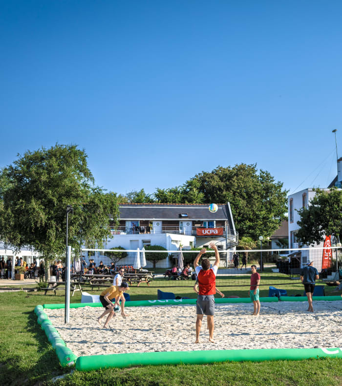 Moniteur et stagiaire en wingfoil à la plage avec voile verte et vagues turquoise en arrière-plan