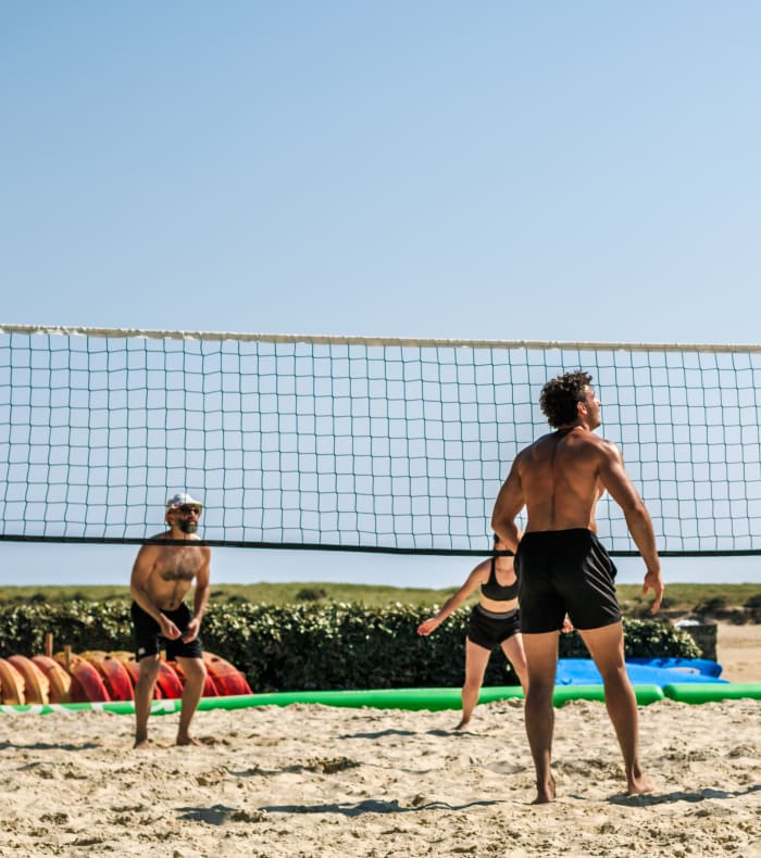 Joueurs de beach-volley en action sur le sable avec filet et ballon lors d'un match au village sportif UCPA