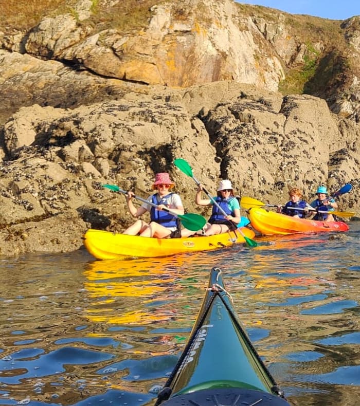 Groupe de kayakistes en kayaks jaunes et bleus pagayant près de rochers sculptés de la Côte d'Émeraude à Saint-Malo