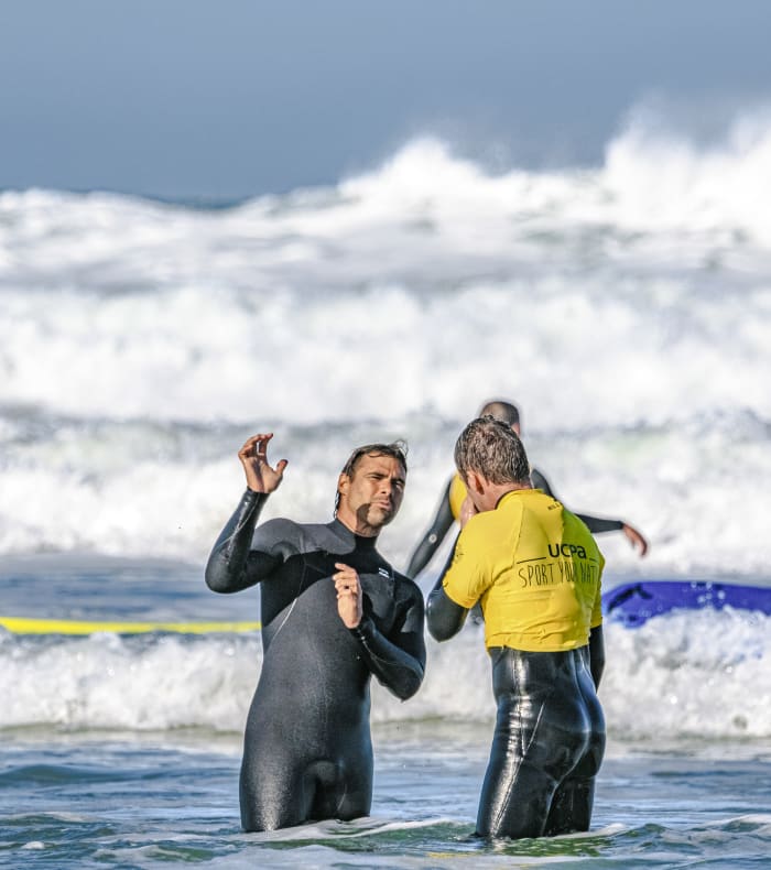 Moniteur de surf en combinaison noire guidant un enfant en gilet jaune dans les vagues du Break 4 jours