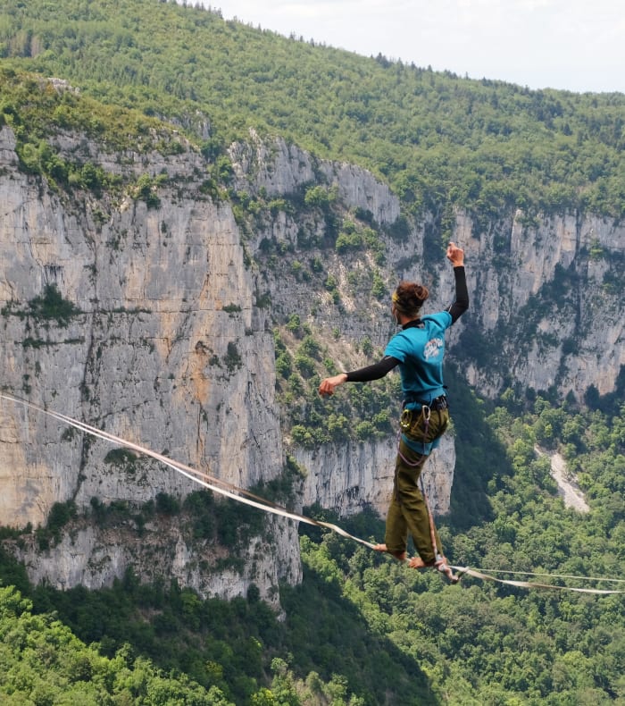 Pratiquant de highline traversant une sangle entre deux falaises calcaires d'Orpierre avec vue panoramique sur la vallée boisée