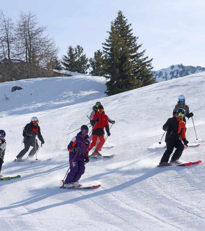 Trois skieurs en tenue colorée dégringolent ensemble sur une piste enneigée des Arcs sous un ciel bleu dégagé
