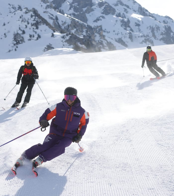 Groupe de skieurs en descente aux Arcs sous un ciel bleu dégagé, pentes enneigées et pics rocheux en arrière-plan