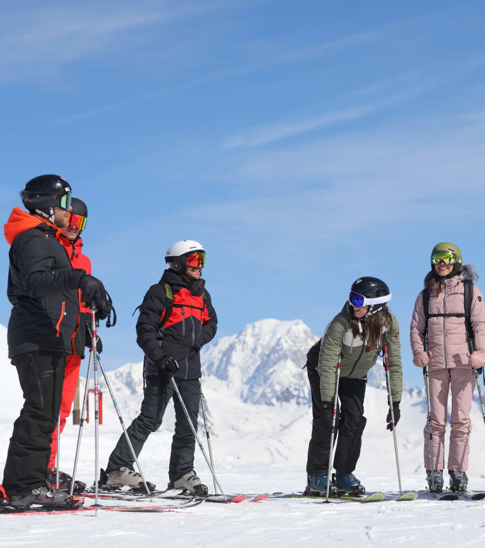 Trois jeunes skieurs assis face aux pistes enneigées des Arcs, skis plantés dans la neige, apprenant le ski en montagne