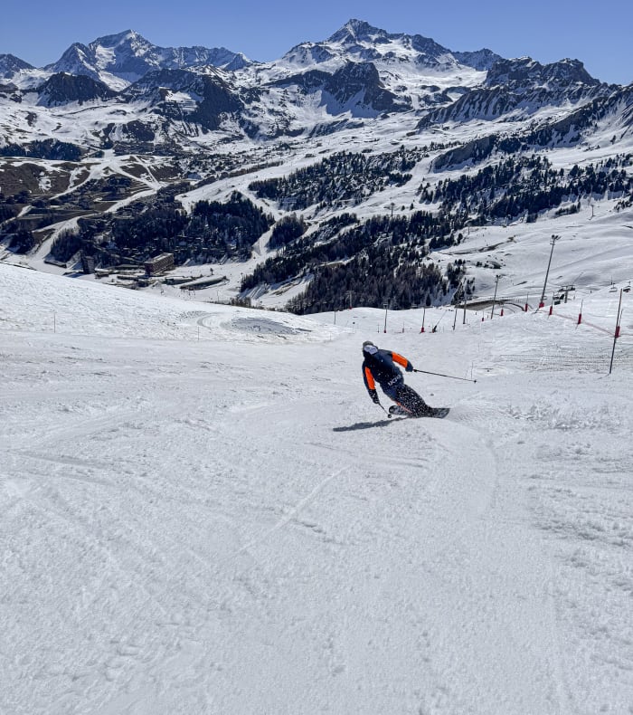 Skieur en monoski descendant une piste enneigée à La Plagne avec sommets alpins et forêts de sapins en arrière-plan