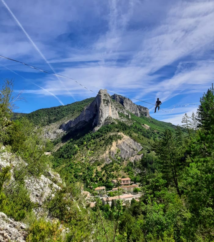 Pratiquant de highline suspendu au-dessus des falaises d'Orpierre avec paysage montagneux boisé