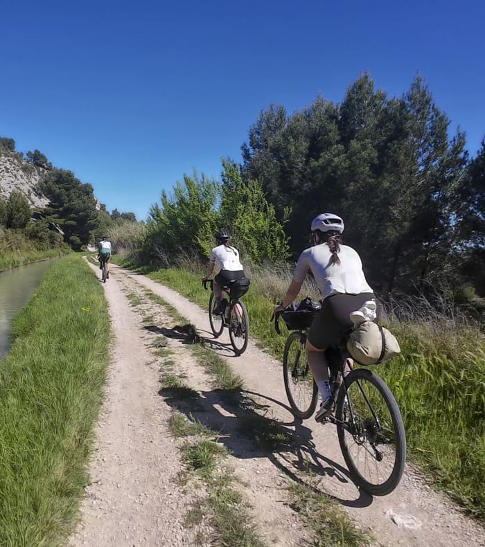 Cyclistes pratiquant le vélo de randonnée sur un chemin de terre longeant un canal, entourés de végétation et de falaises calcaires