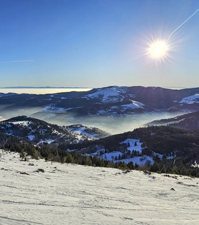 Randonnée hivernale en raquettes aux Vosges avec vue sur pentes enneigées et forêt de sapins sous ciel bleu