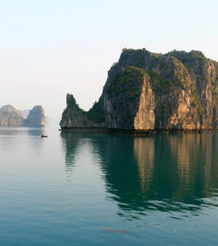 Baie du Tonkin avec formations calcaires émergeant des eaux turquoise et petit bateau traditionnel vietnamien