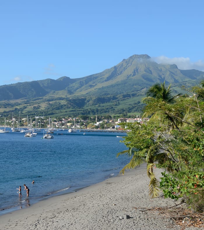 Baie de Saint-Pierre en Martinique avec plage de sable, voiliers ancrés et montagne verdoyante en arrière-plan