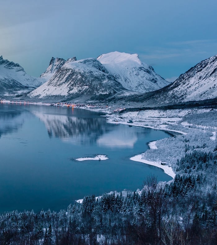 Paysage arctique enneigé avec lac gelé, montagnes majestueuses et forêts de mélèzes en Laponie norvégienne