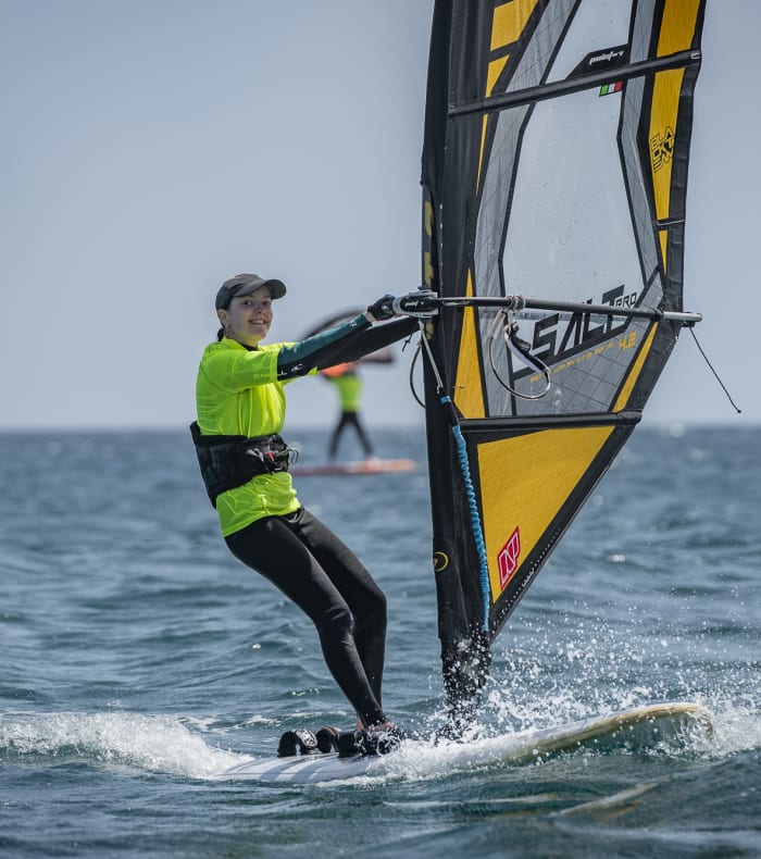 Windsurfeur en gilet de sauvetage jaune naviguant sur la mer Méditerranée avec voile jaune et noire