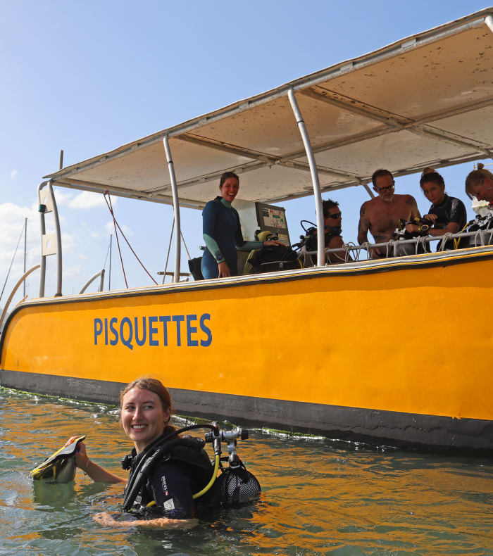Plongeur en combinaison équipé sortant de l'eau près du bateau Pisquettes aux Saintes avec groupe de plongeurs à bord