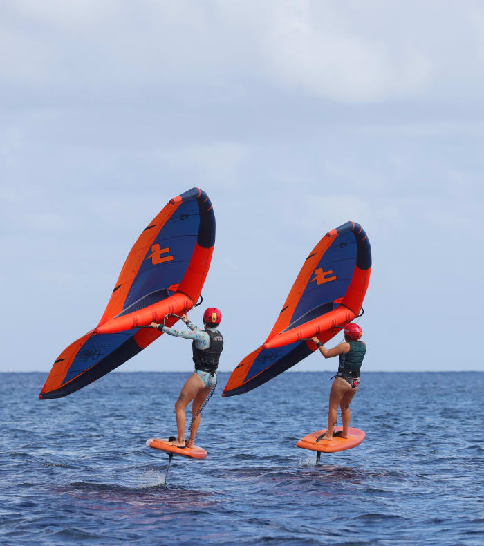 Trois jeunes pratiquant le wingfoil et le wakeboard en Gironde avec voiles rouges et bleues sur l'eau