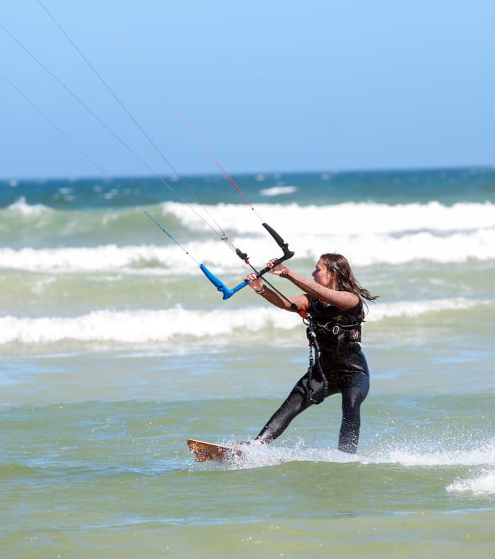 Kitesurfeur en progression effectuant un waterstart avec cerf-volant bleu sur une plage d'Afrique du Sud avec vagues et ciel dégagé