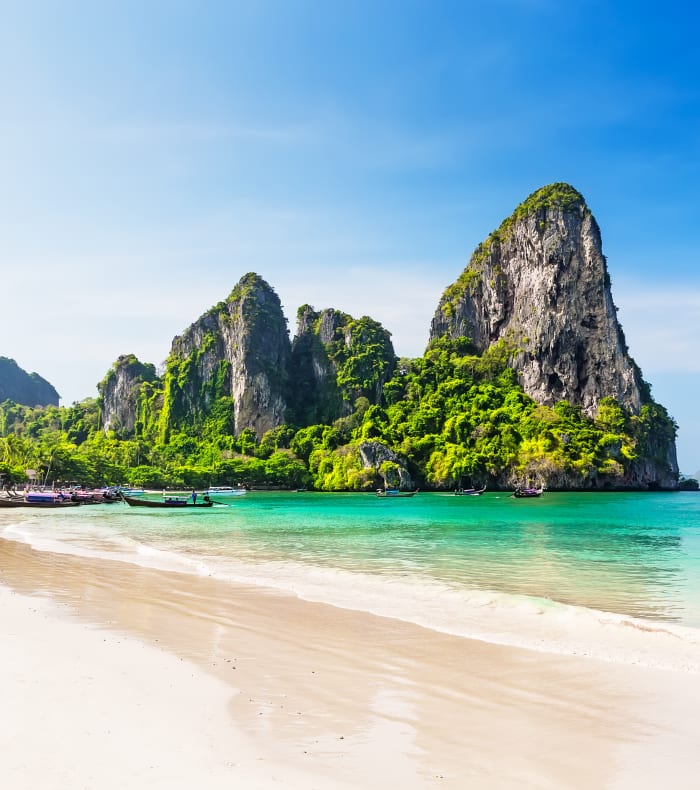 Plage de Krabi en Thaïlande avec falaises calcaires, eau turquoise et barque traditionnelle