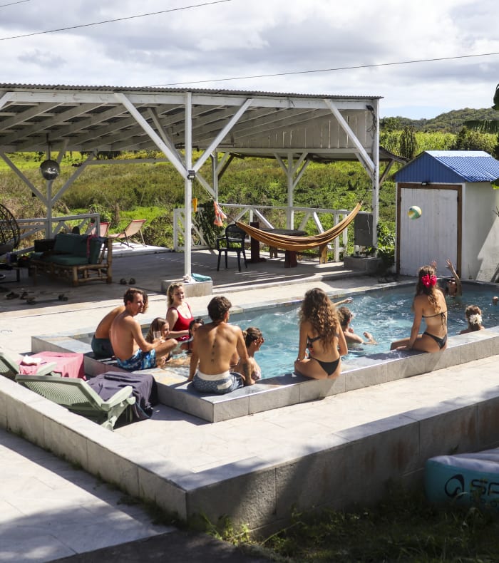 Surf House Le Moule en Guadeloupe avec piscine, groupe de surfeurs se relaxant sous pergola et équipements de sports nautiques