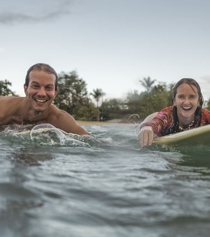 Deux surfeurs souriants en eau tropicale avec planche de surf lors d'un séjour de surf en Guadeloupe
