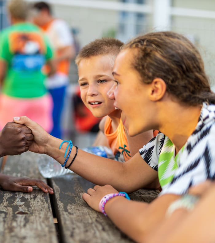 Enfants en internat jouant à un jeu de coopération autour d'une table en bois, se donnant la main dans une activité collective d'entraide et de confiance