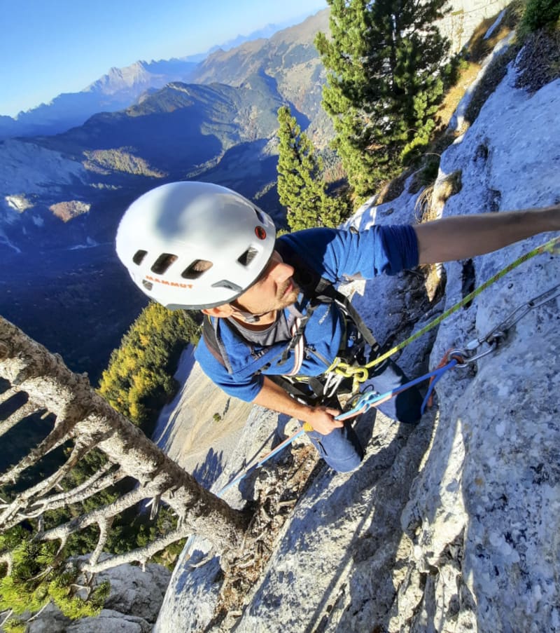 Grimpeur en grande voie équipé d'un casque blanc sur une falaise calcaire de la Drôme avec vallée alpine en arrière-plan