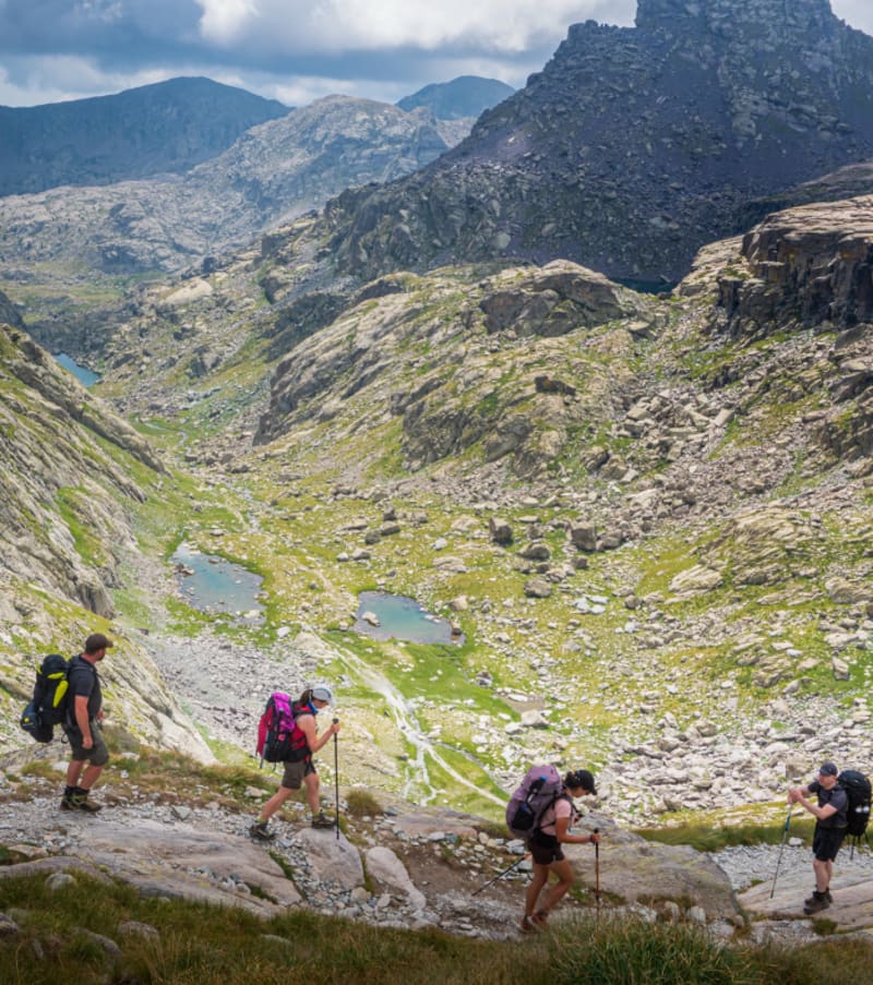 Randonneurs en groupe traversant la Vallée des Merveilles avec sommets rocheux et lacs alpins en arrière-plan