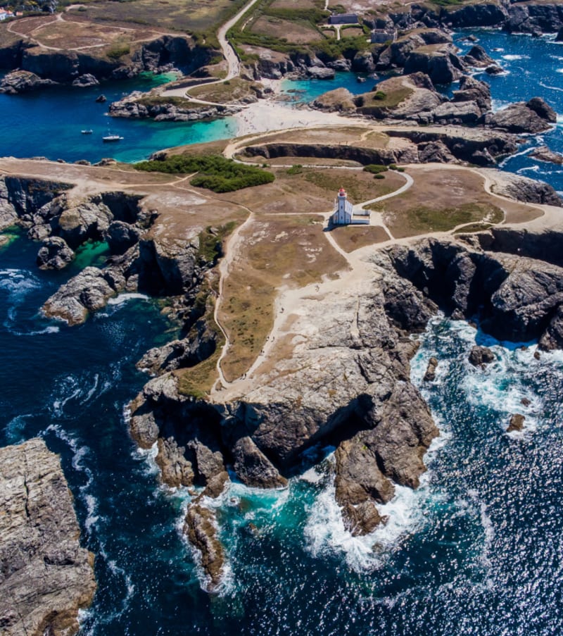 Vue aérienne de Belle-Île avec falaises rocheuses, sentiers côtiers et phare dominant la mer turquoise bretonne